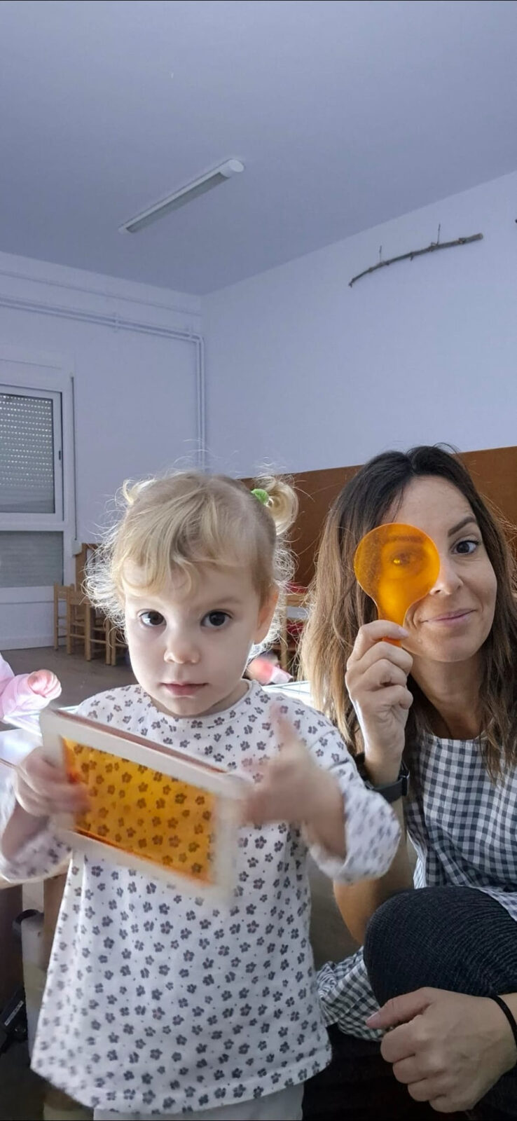Vanesa en el aula con una niña pequeña que juega con láminas de colores